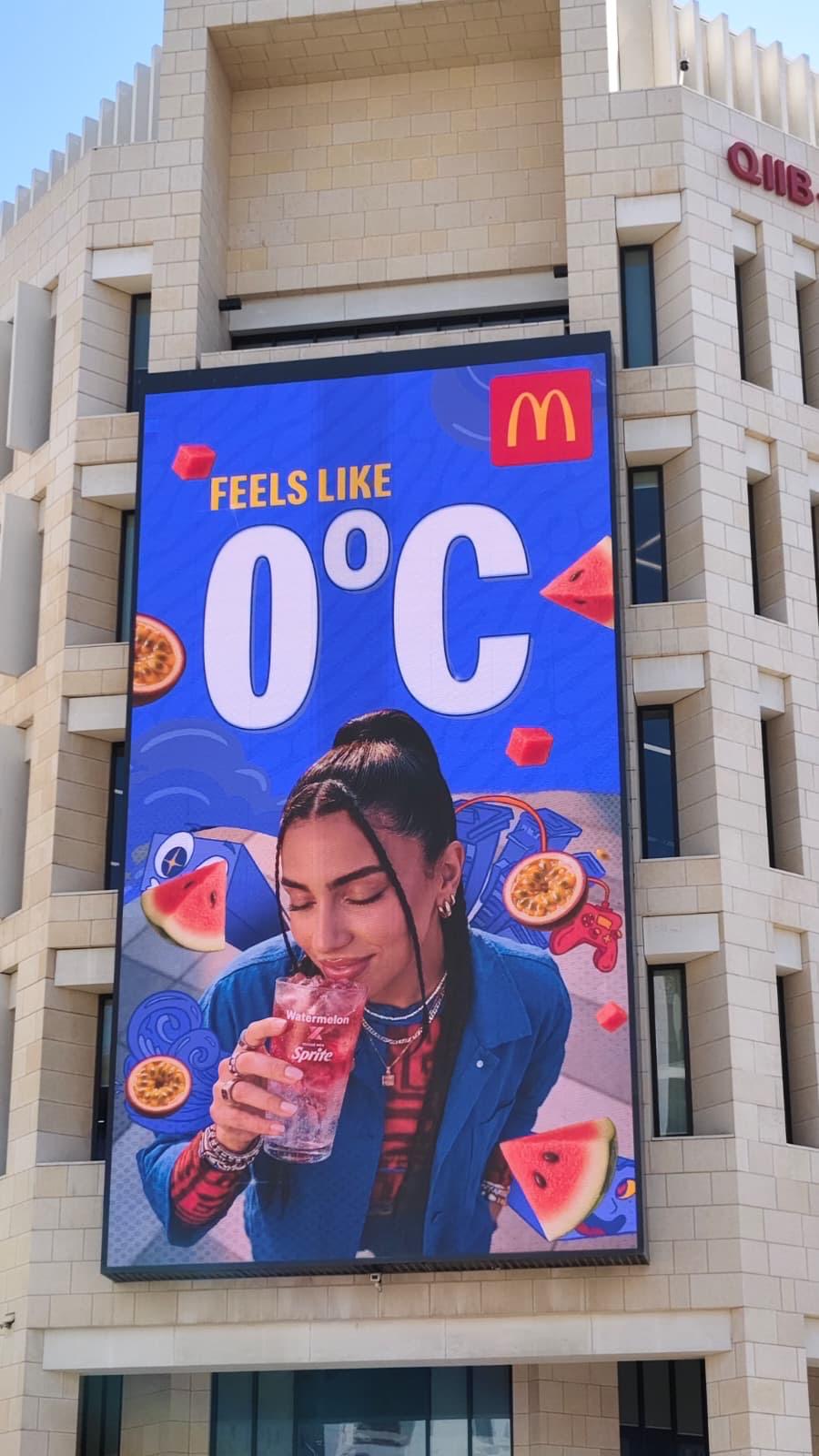 McDonald's weather-reactive digital billboard on a Doha tower reading FEELS LIKE 0°C over a Watermelon Sprite, part of the nine-screen ELAN Media network.
