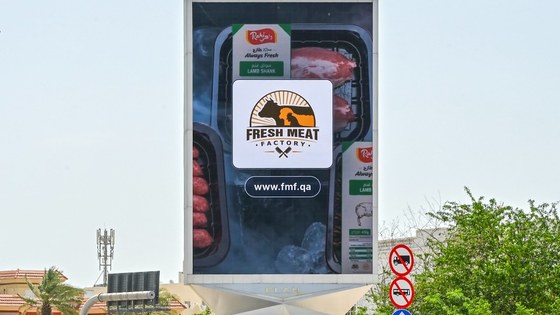 A tall roadside screen in Qatar showing the Fresh Meat Factory board over packaged lamb, with the fmf.qa address.